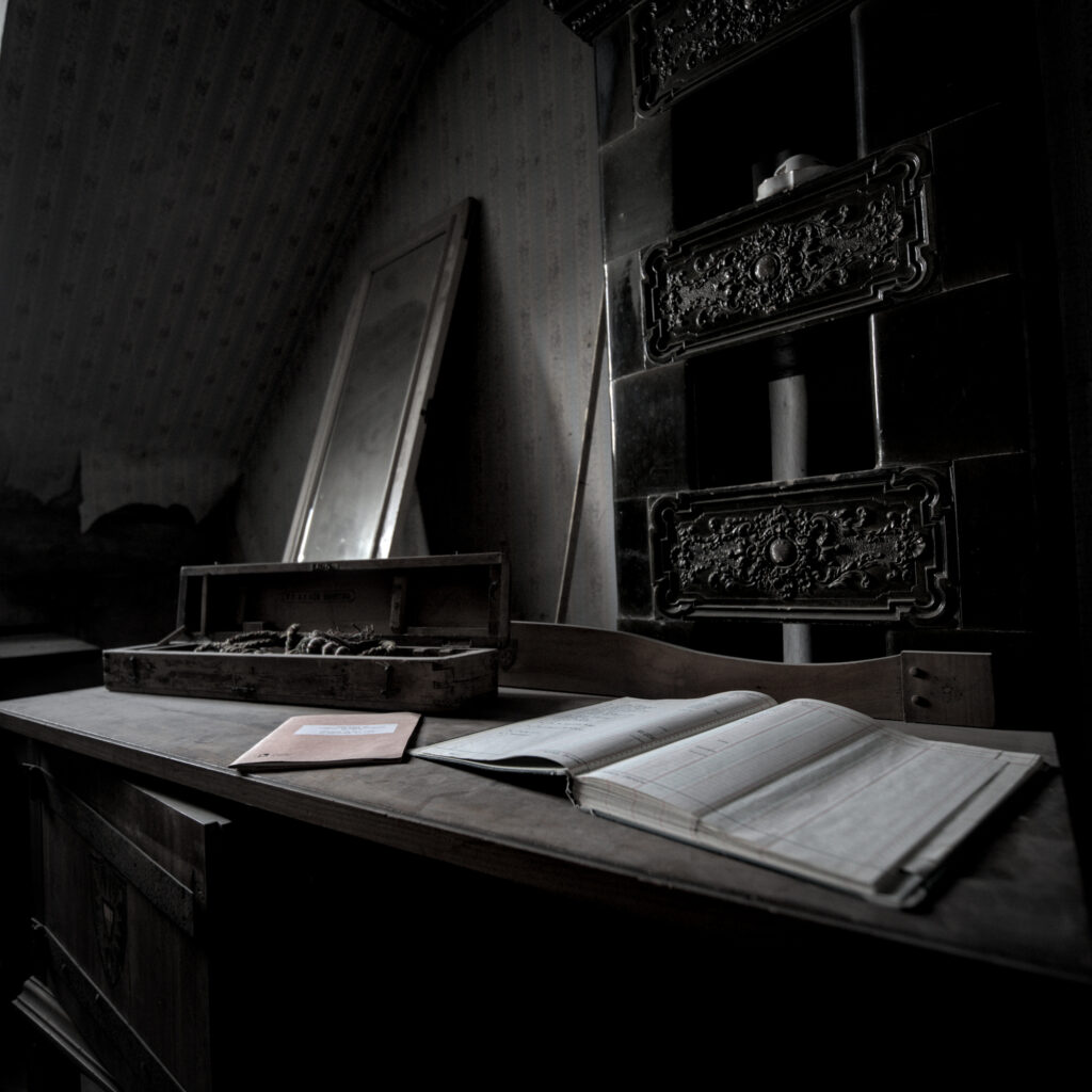 Auf einem Schreibtisch liegt ein geöffnetes Buch. Dahinter ein Holzkasten