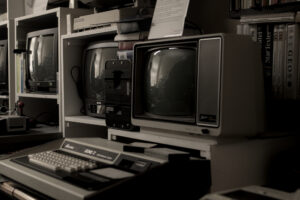 In einem Ausstellungsraum. Drei Röhrernbildschirme auf einem Schreibtisch. Davor jeweils ein Historischer Computer