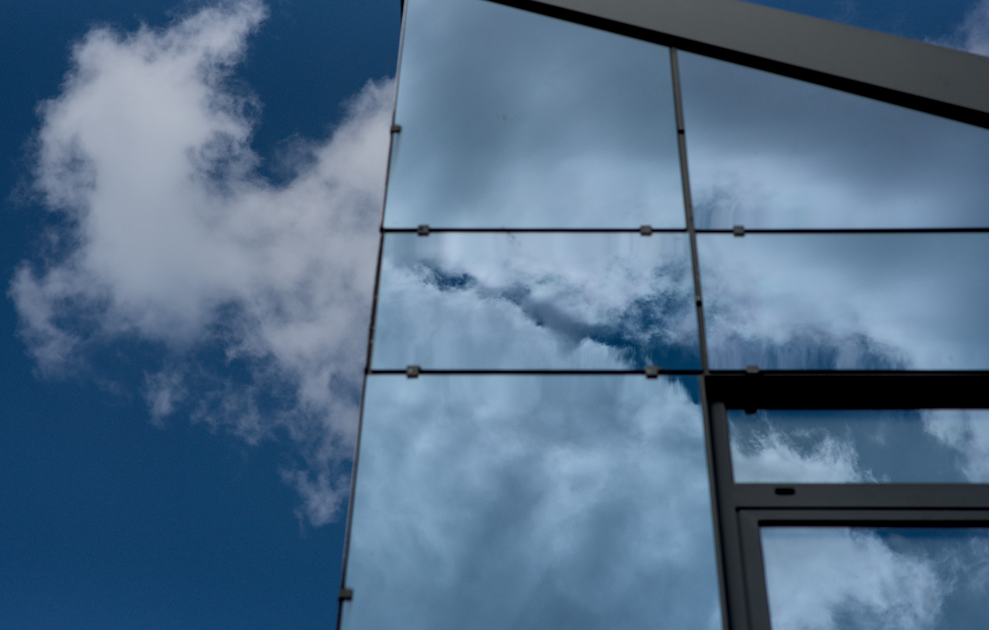 Eine Fensterfront in der sich Wolken spiegeln