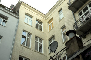 Blick in einen Innenhof zwischen zwei weißen Gebäuden. Ein gelbes Gebäude mit Balkonen ist im Hintergrund sichtbar. Ein Teil eines weißen Zeltes ist im Vordergrund.